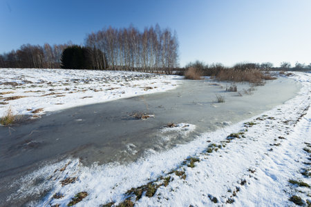 Frozen snow and water on a rural field, sunny winter dayの写真素材