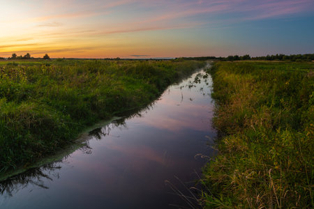 A view of a small, quiet river in eastern Poland during sunsetの写真素材