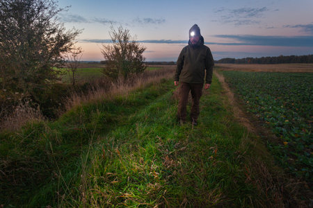 A man with a headlamp walks along a country road on a cool eveningの写真素材