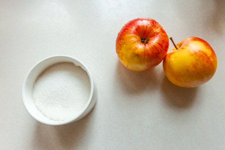 White sugar in a sugar bowl and two washed apples on the tableの写真素材