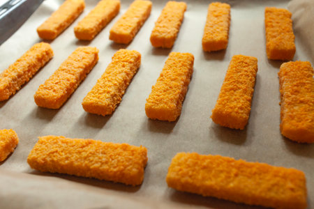 Fish fingers in golden breadcrumbs placed on paper and a baking trayの写真素材