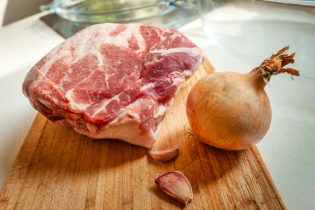 A piece of raw meat on a wooden board with onion and garlic
