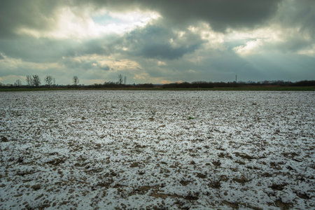 A cloudy sky over a plowed and snow-covered rural fieldの写真素材