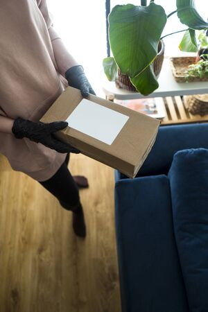 Young blonde girl in protective gloves holding cardboard boxes. Epidemic. Coronavirus. Covid-19. Quarantine. Shipping parcel during coronavirus time. Opening a package during a pandemic in home.の写真素材