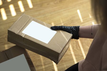 Young blonde girl in protective gloves holding cardboard boxes. Epidemic. Coronavirus. Covid-19. Quarantine. Shipping parcel during coronavirus time. Opening a package during a pandemic in home.の写真素材