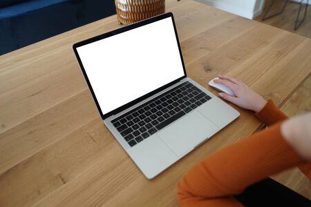 Young woman working on laptop. Laptop on wooden desk with white screen. Green plant in background. Mockup for web design. Close up.の写真素材