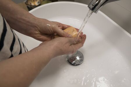 COVID-19 Coronavirus. Woman washing hands with foam soap and hot water at bathroom. Hygiene, preventing coronavirus. Corona Virus pandemic protection by cleaning hands frequently.の写真素材