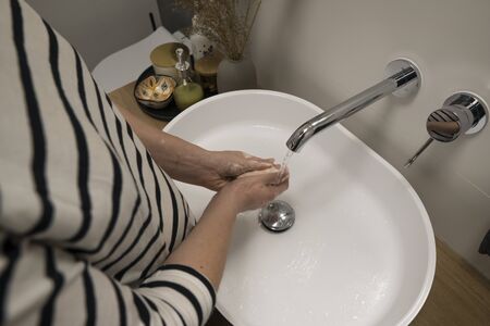 COVID-19 Coronavirus. Woman washing hands with foam soap and hot water at bathroom. Hygiene, preventing coronavirus. Corona Virus pandemic protection by cleaning hands frequently.の写真素材