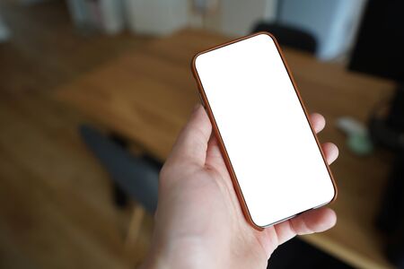 Working on mobile. Taking a picture. Phone in hand with white screen. Blur background. Mockup for mobile design. Close up.の写真素材