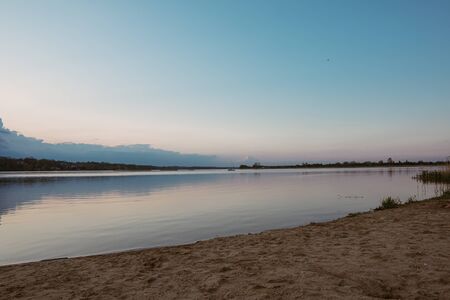 Landscape of a lake with a happy dog or mongrel running. Beautiful sky with clouds during sunset. Sandy beach. Free time. Free time during a pandemic COVID-19 coronavirus and quarantine.の写真素材