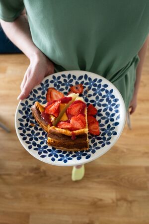 Cheesecake with fresh strawberries and strawberry sauce. A delicious dessert on a colorful plate in the hands of a young girlの写真素材