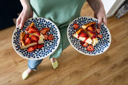 Cheesecake with fresh strawberries and strawberry sauce. A delicious dessert on a colorful plate in the hands of a young girlの写真素材