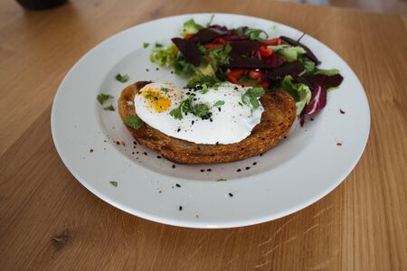 Poached egg on a piece of bread with green salad on a plate and on the wooden table. Healthy Breakfastの写真素材