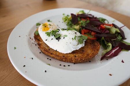 Poached egg on a piece of bread with green salad on a plate and on the wooden table. Healthy Breakfastの写真素材