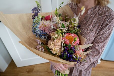 Beautiful bouquet of mixed blossoming fresh flowers in woman hands. Florist with delicate colorful boho style bouquet of peony, gillyflower, eustoma, clove branch, dill, sea lavender, gerberaの写真素材