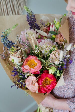 Beautiful bouquet of mixed blossoming fresh flowers in woman hands. Florist with delicate colorful boho style bouquet of peony, gillyflower, eustoma, clove branch, dill, sea lavender, gerberaの写真素材