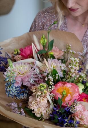 Beautiful bouquet of mixed blossoming fresh flowers in woman hands. Florist with delicate colorful boho style bouquet of peony, gillyflower, eustoma, clove branch, dill, sea lavender, gerberaの写真素材
