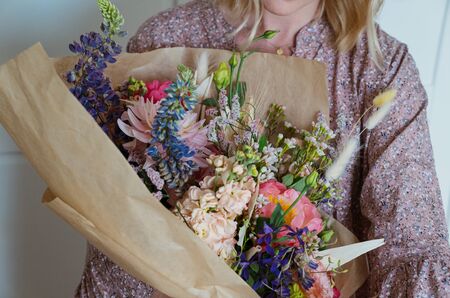 Beautiful bouquet of mixed blossoming fresh flowers in woman hands. Florist with delicate colorful boho style bouquet of peony, gillyflower, eustoma, clove branch, dill, sea lavender, gerberaの写真素材