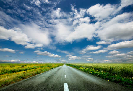 image of wide open prairie with a paved highway stretching out as far as the eye can see with beautiful small green hills under a bright blue sky in the summer time