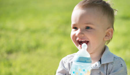 The kid drinks water from a bottle with a pacifier on the nature.の写真素材