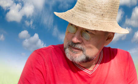 A man with a beard, in a golden pince-nez of the 19th century, wearing a straw hat on the blue of the blue skyの写真素材