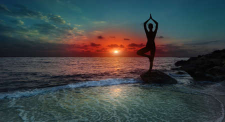 Silhouette young woman practicing yoga on the beach at sunset.の写真素材