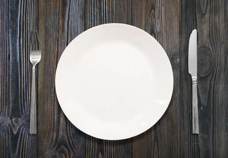 White plate, knife, fork, on a background of wood