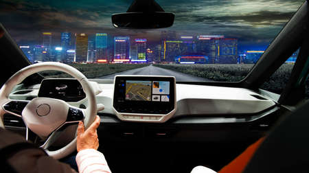 Two women driving a super modern car on an asphalt highway towards a night city.の写真素材
