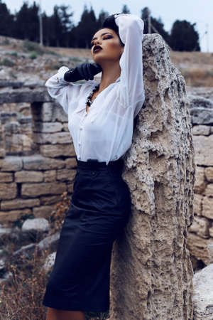 Fashion outdoor photo of sexy elegant woman with dark hair wearing a white shirt, black leather...