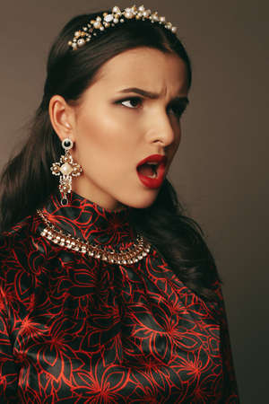 fashion studio portrait of gorgeous woman with dark hair and bright makeup wears luxurious elegant black and red dressの写真素材