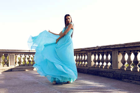 fashion outdoor photo of gorgeous woman with dark hair wears luxurious elegant dress, posing near antic palaceの写真素材