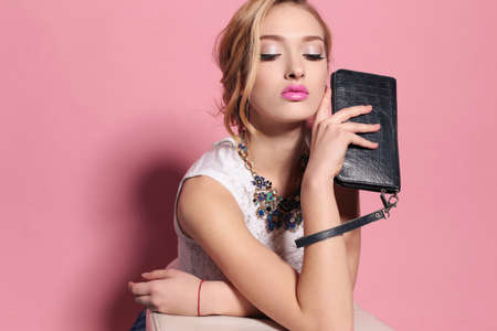fashion studio photo of gorgeous young woman with blond curly hair wears elegant lace dress and luxurious necklace,holding small bag in handsの写真素材