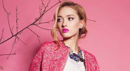 fashion studio photo of gorgeous young woman with blond curly hair wears elegant pink coat,blouse and luxurious necklaceの写真素材