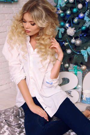 fashion interior photo of beautiful woman with blond hair  in elegant clothes,posing  at cozy home, with presents and New Year decorationの写真素材