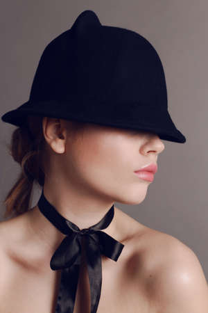 fashion studio photo of beautiful woman with dark hair wears elegant black hat and silk bow on neckの写真素材