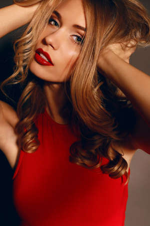 Fashion photo of beautiful lady with blond curly hair and bright evening makeup, wears elegant...