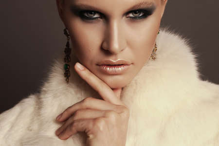 fashion photo of glamour beautiful woman with blond hair and smokey eyes makeup,wears luxurious fur...