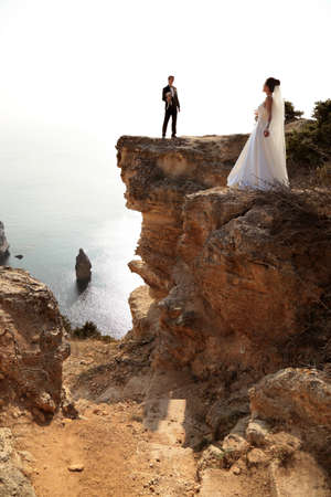 fashion outdoor photo of beautiful couple. gorgeous bride in wedding dress posing with elegant groom on sea costの写真素材