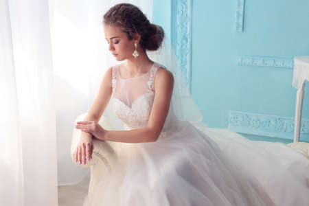 fashion studio photo of beautiful young bride with dark curly hair in luxurious wedding dress posing at roomの写真素材