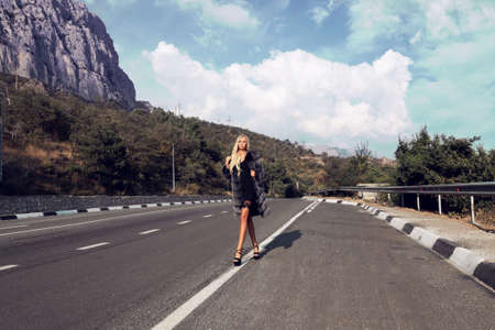 fashion outdoor photo of gorgeous sexy woman with long blond hair in casual clothes and fur posing on roadの写真素材