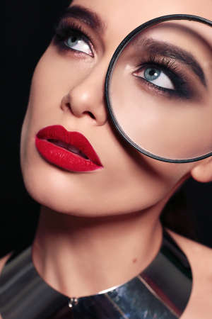 fashion studio portrait of gorgeous sexy woman with dark hair and bright makeup, using magnifier