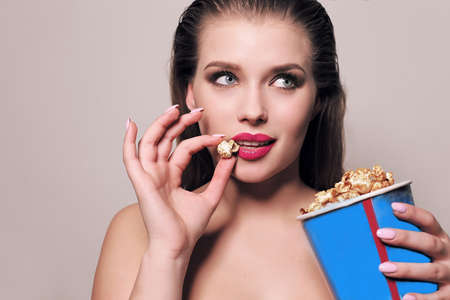 fashion studio photo of beautiful young woman with dark hair posing with popcorn bucket