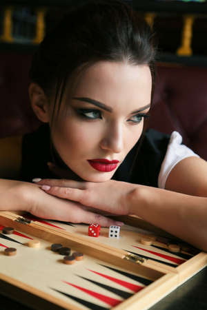 fashion portrait of beautiful girl with dark hair and bright red lips makeup, holding play dice