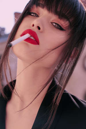 fashion photo of gorgeous woman with dark hair in elegant clothes posing at studio, smoking cigaretteの写真素材