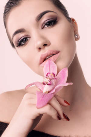 fashion studio portrait of beautiful young girl with dark hair and bright makeup, holding flower in handsの写真素材