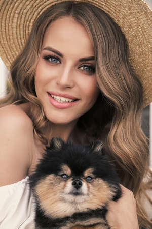 fashion outdoor photo of gorgeous girl with dark hair in elegant clothes, holding small cute puppyの写真素材
