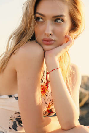 fashion outdoor photo of beautiful girl with blond hair in elegant clothes posing at summer sunset beachの写真素材