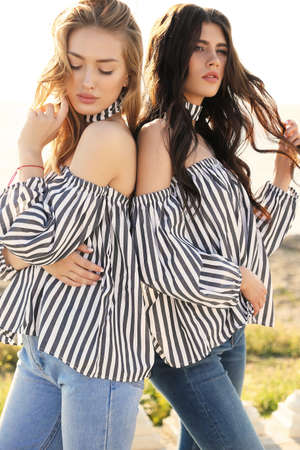 fashion photo of two beautiful girls in casual clothes posing outdoorの写真素材