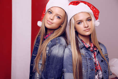 fashion interior photo of beautiful girls with blond hair in Santa hat posing near Christmas presentsの写真素材