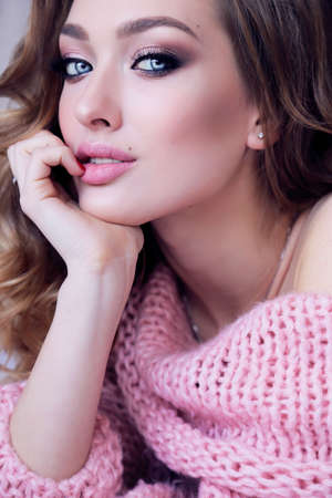 fashion photo of beautiful young girl with blond curly hair in cozy clothes posing in studioの写真素材